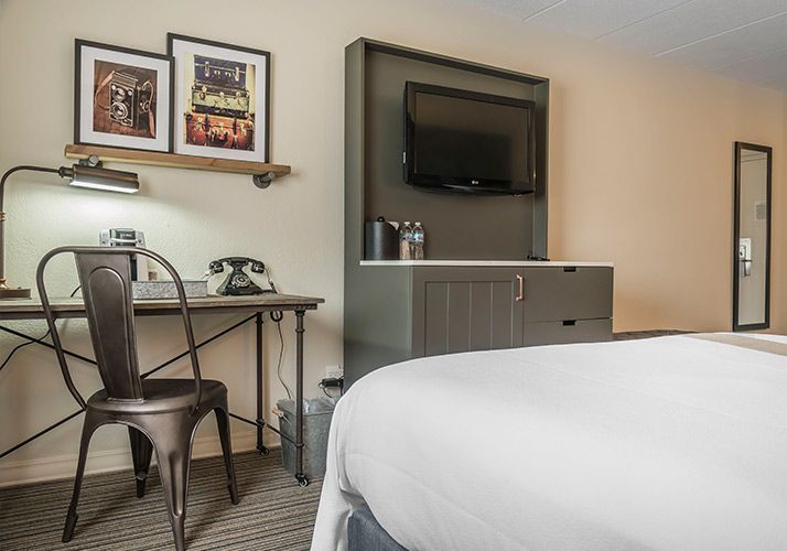 Hotel room with desk, chair, wall-mounted TV, and a bed in the foreground