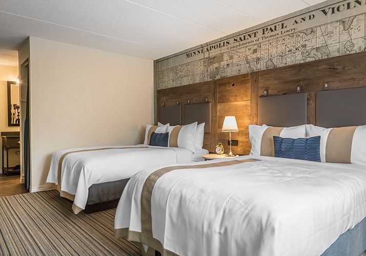 Two neatly made queen beds in a modern hotel room with a wood accent wall and bedside lamps