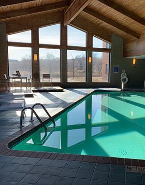 Indoor pool with turquoise water, sunlight through large windows, and a high wooden ceiling