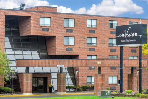Brick hotel exterior with “Hilton” sign, large windows, and covered entrance under a partly cloudy sky