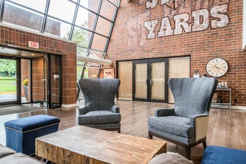 Brick lobby lounge with two gray chairs, blue ottomans, wooden table, and wall clock at The Yards.