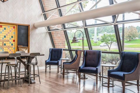 Modern lounge with blue chairs, tall stools, wood floor, and large windows overlooking a golf course.