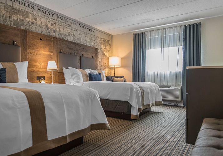 Hotel room with three neatly made beds, warm lamps, and a large window with curtains