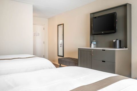 Hotel room with two twin beds, wall-mounted TV, dresser, mirror, and a bench.