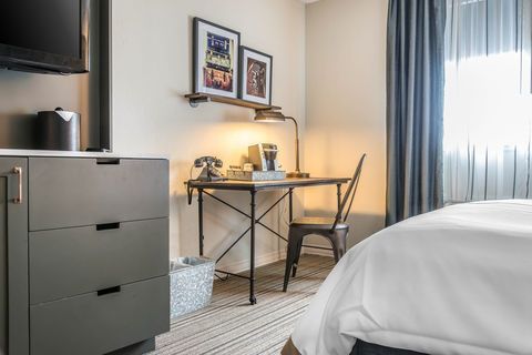 Modern bedroom with desk, chair, dresser, bed, and window with blue curtains