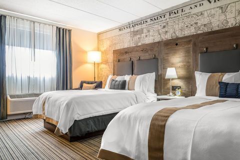 Hotel room with two white beds, warm bedside lamp, and large window with sheer curtains