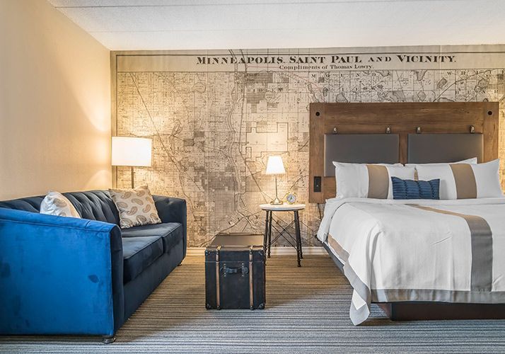 Modern hotel room with blue sofa, bed, bedside lamps, and wall map mural