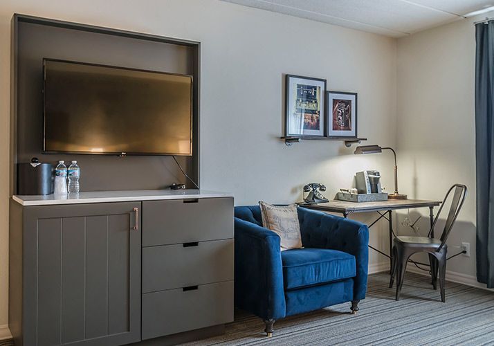 Hotel room with TV, cabinet, blue chair, desk, and two chairs by a window