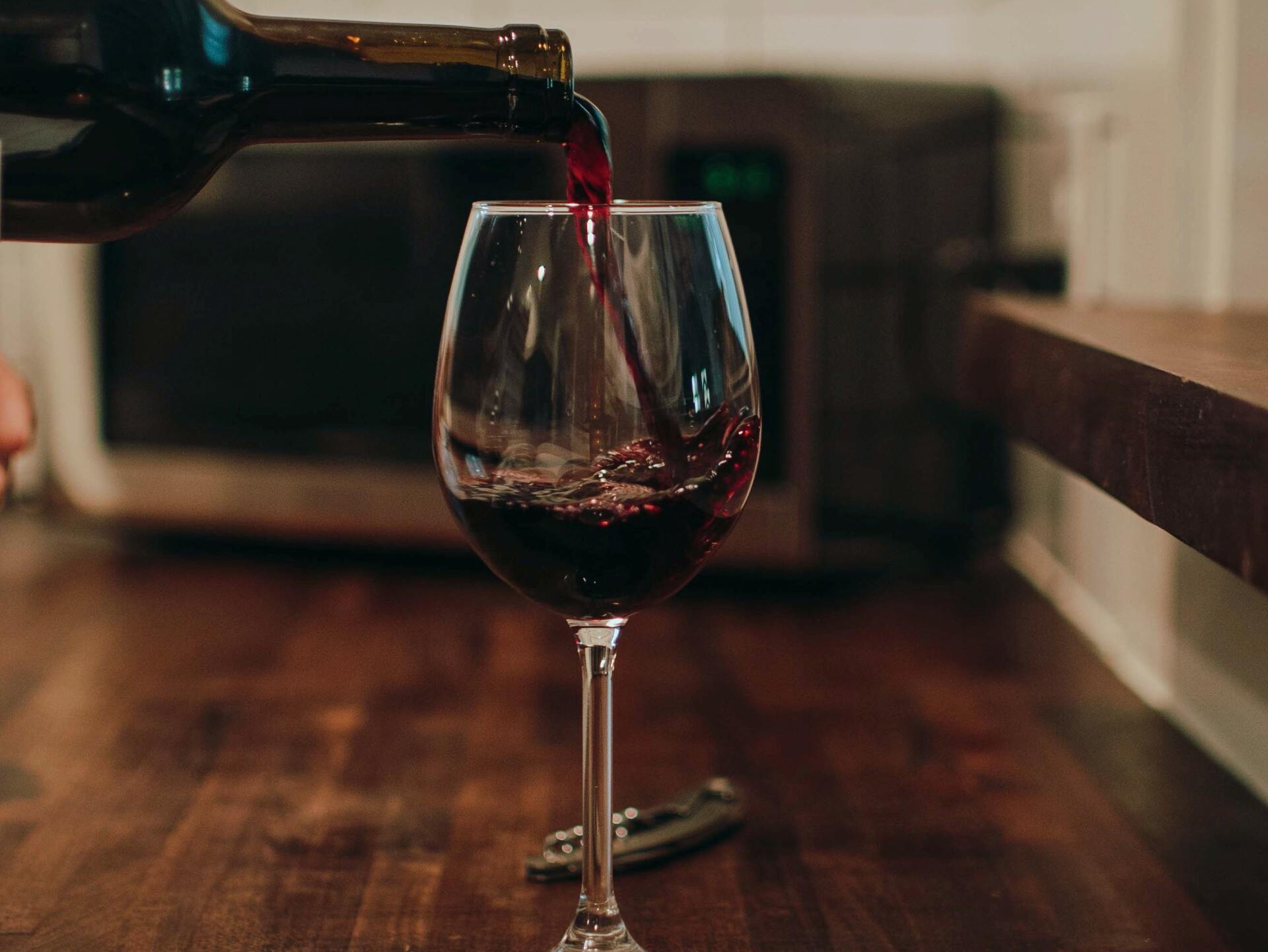 Red wine being poured into a wine glass on a wooden table.