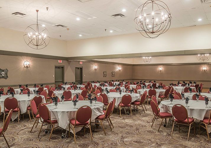 Banquet hall with round tables draped in white, red chairs, and hanging chandeliers before an event