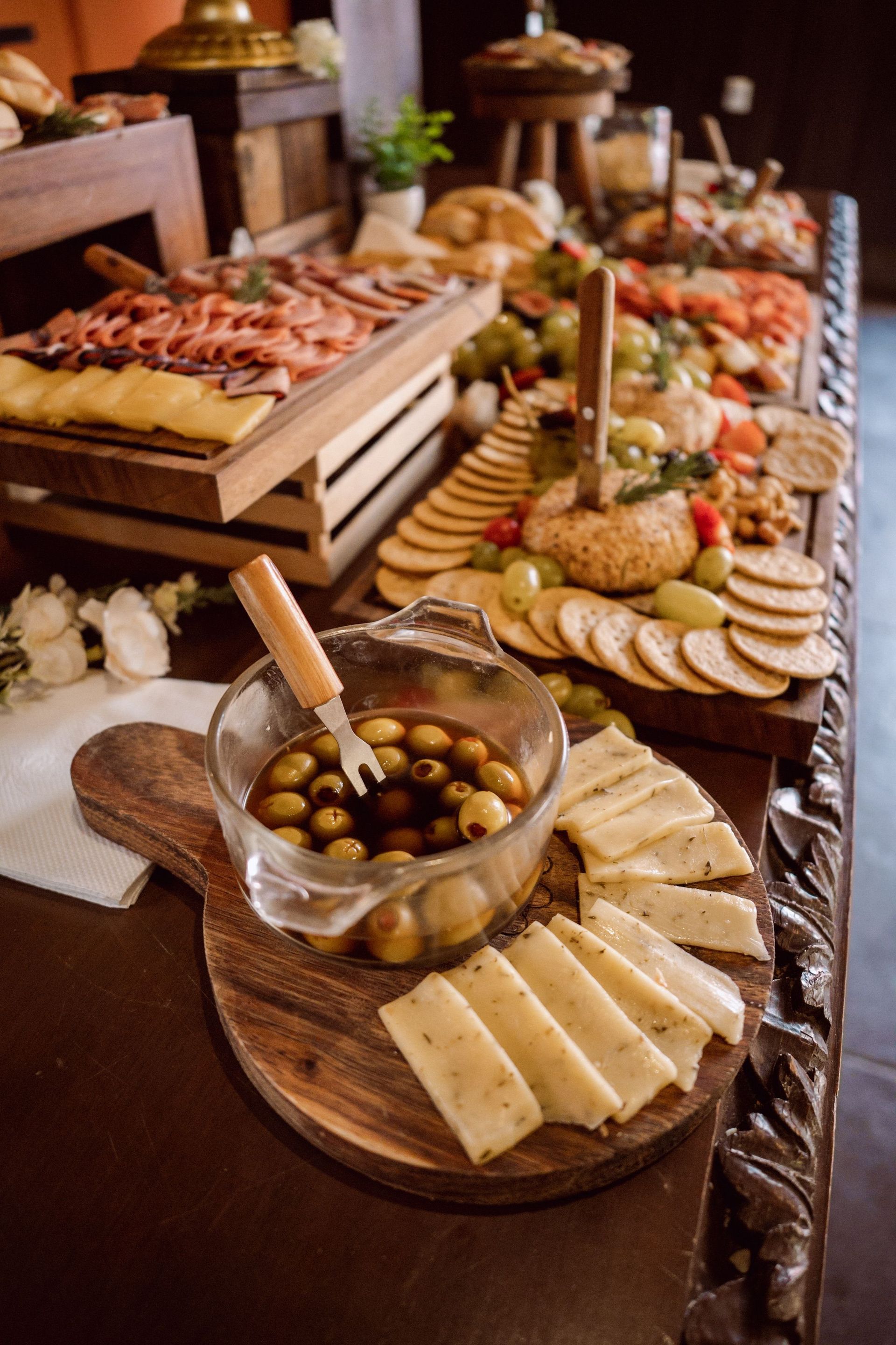 Buffet table with assorted appetizers, bread, olives, and cheese on wooden platters
