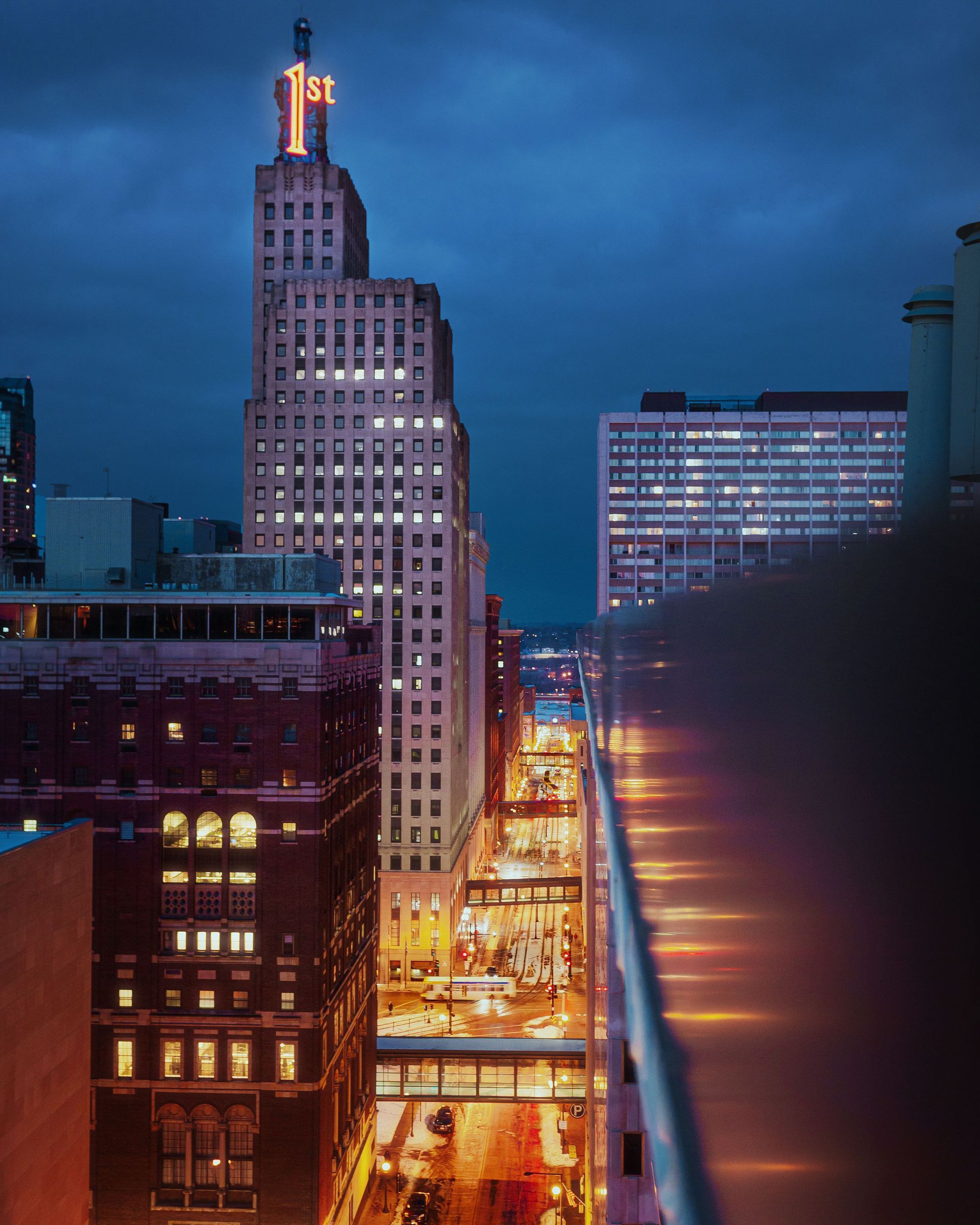 Downtown skyscraper at dusk beside a lit waterfront promenade