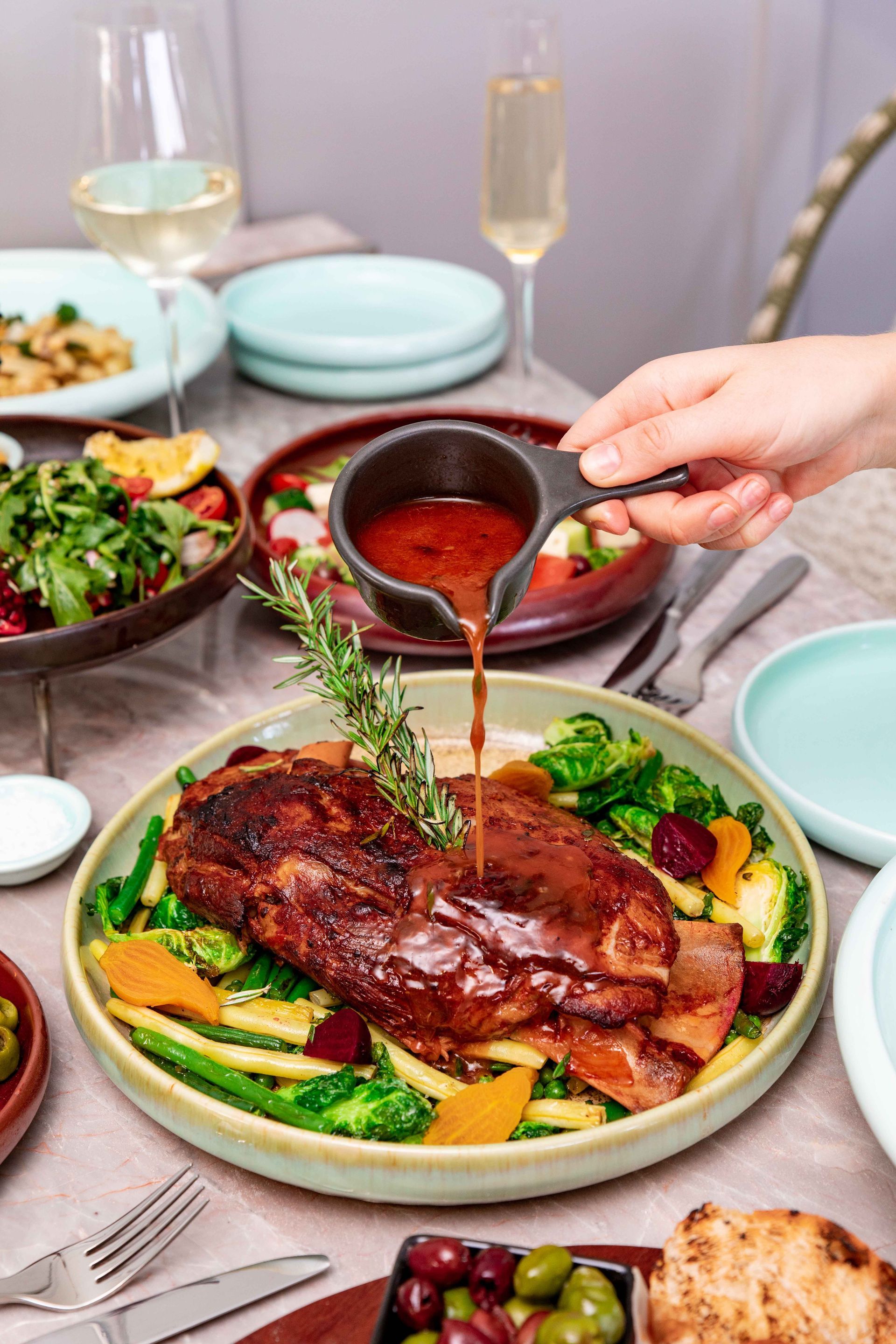 Roasted meat with sauce poured over, served on a colorful dinner table with wine glasses and side dishes