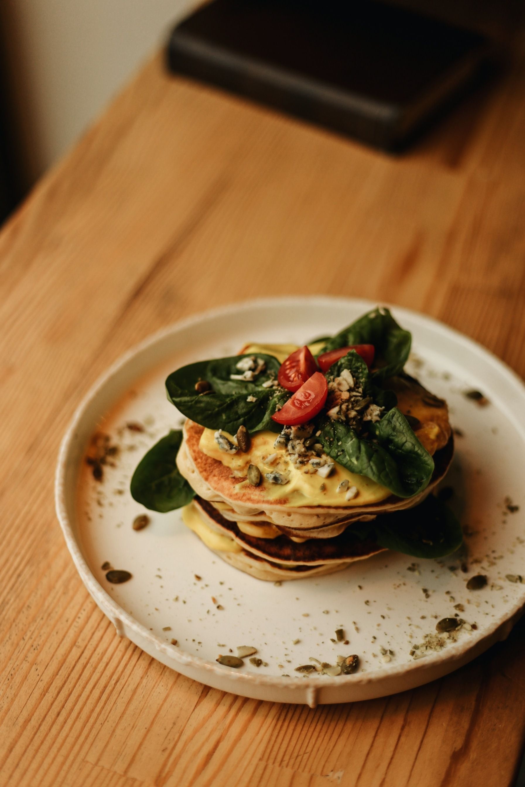 Stack of pancakes topped with spinach and cherry tomatoes on a white plate on a wooden table