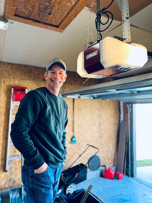A man is standing in a garage next to a garage door opener.