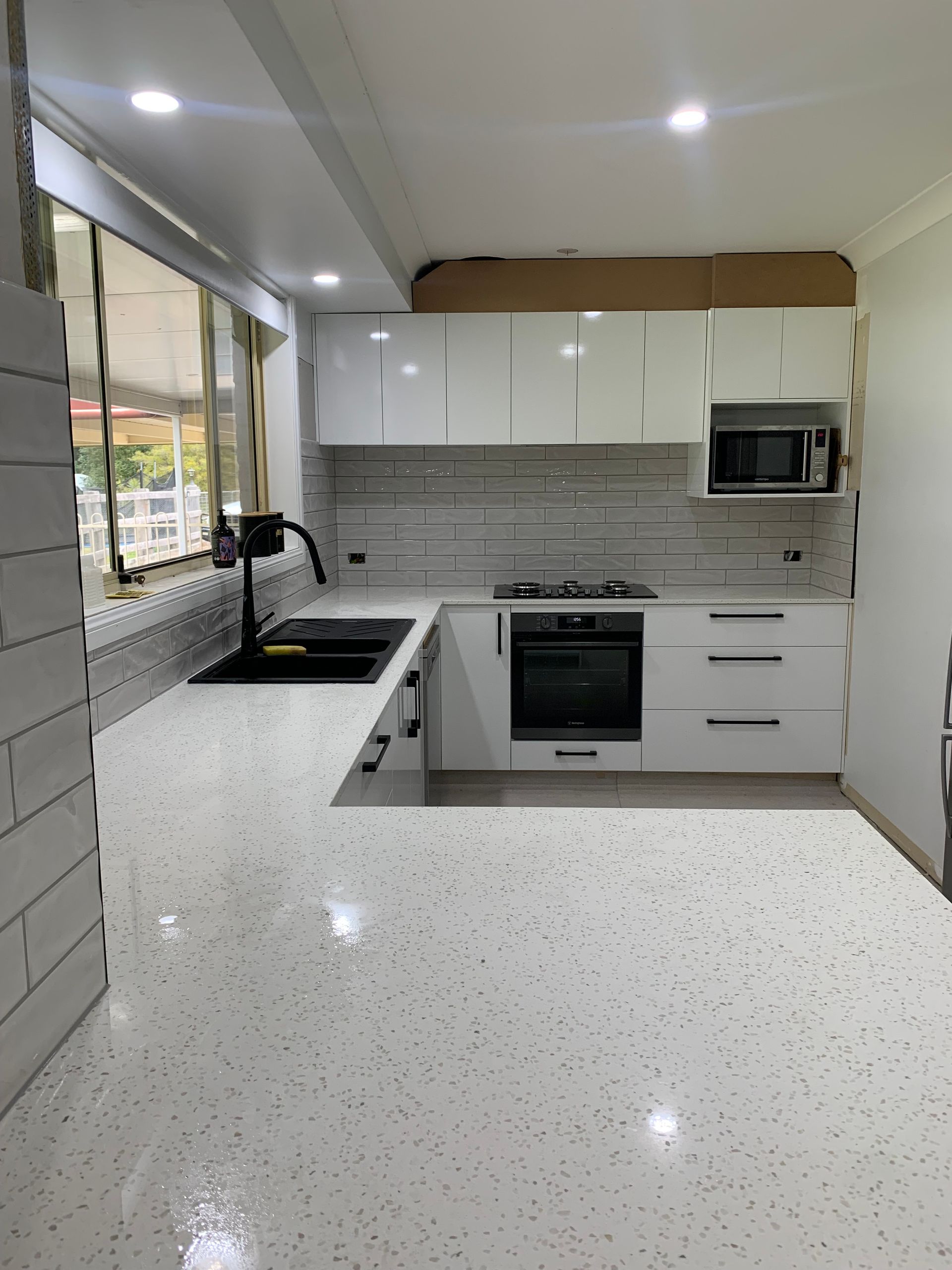 Modern White Kitchen With Speckled Countertop — Midcoast Wall & Floor Tiling in Woolgoolga, NSW