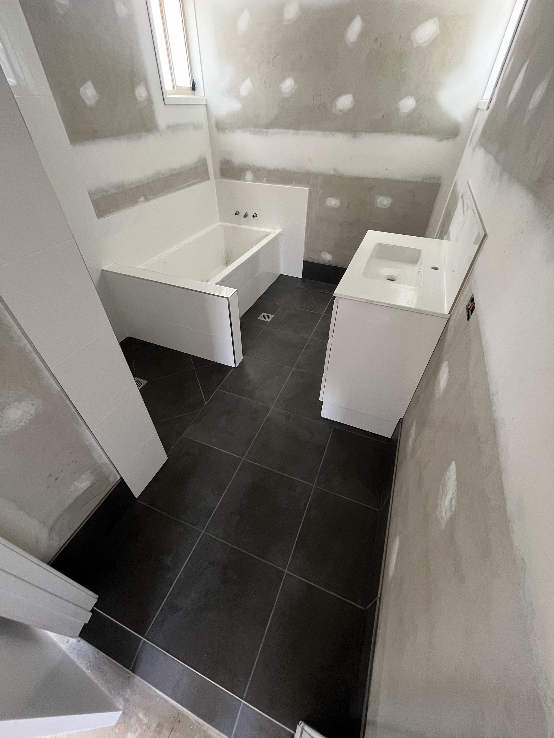 Narrow Unfinished Bathroom With Dark Tile Floor — Midcoast Wall & Floor Tiling in Woolgoolga, NSW