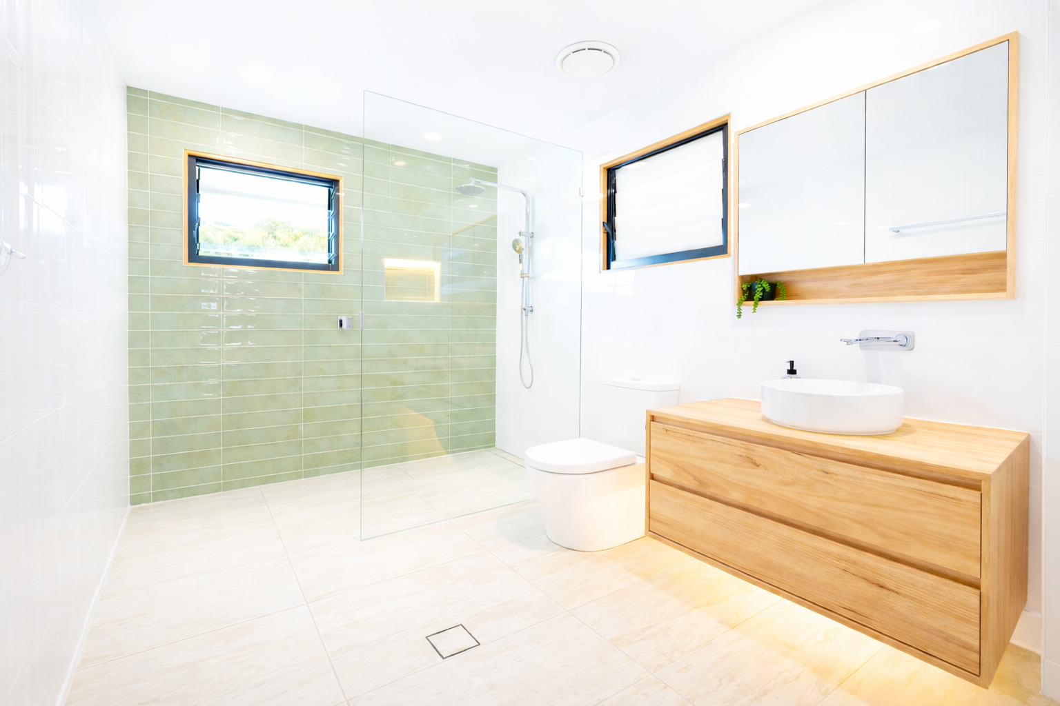 A bathroom with terrazzo tile floors, a white double vanity, black cabinets, and a white toilet next to a glass shower.
