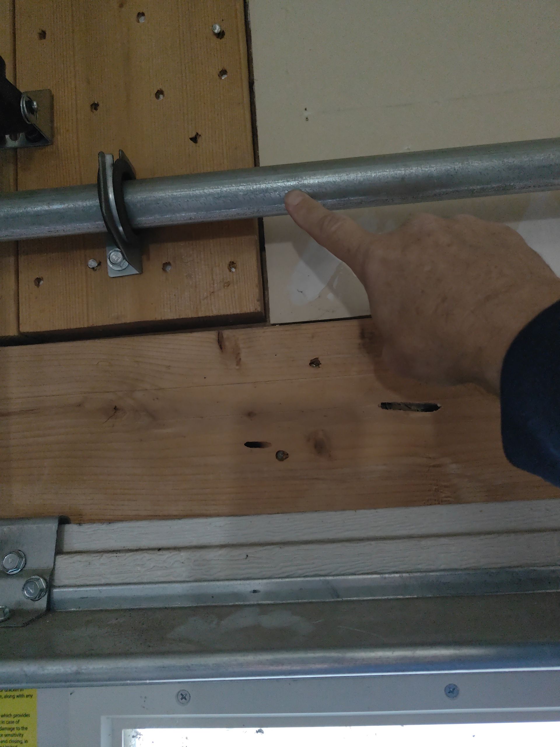 Finger pointing at a metal pipe mounted on a wooden wall or garage door.