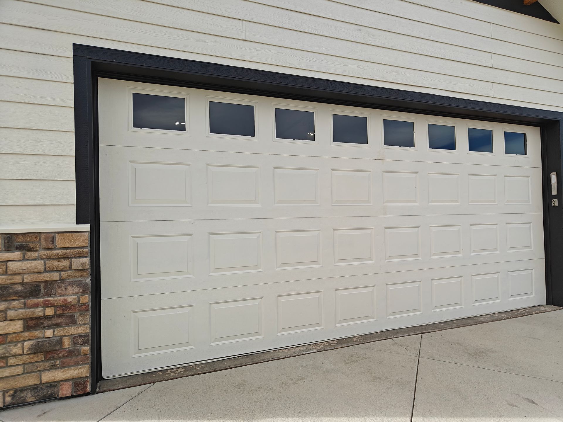 White garage door with small square windows, set in a light-sided building with stone trim.
