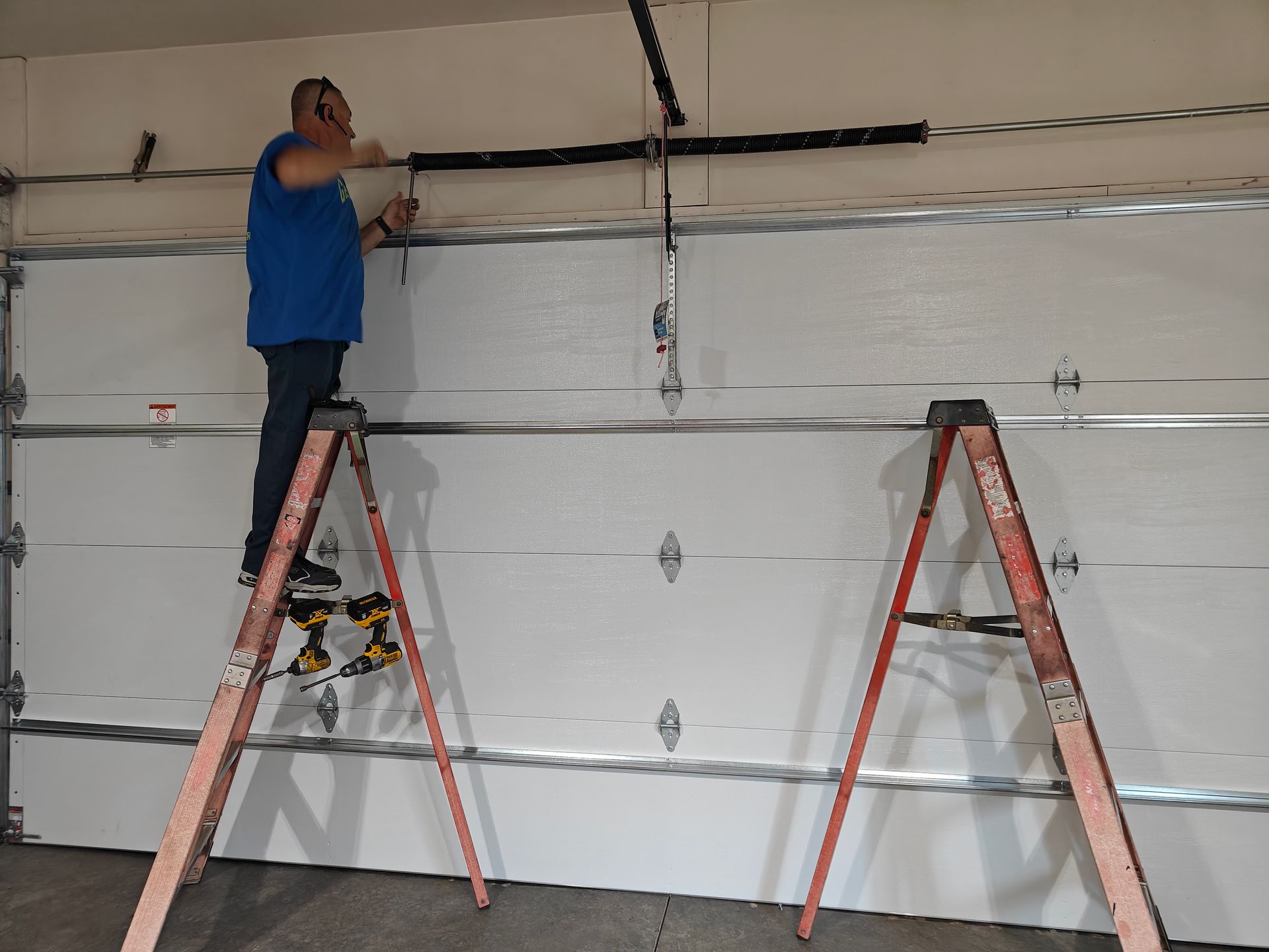 Worker on ladder installing garage door tracks inside a white garage