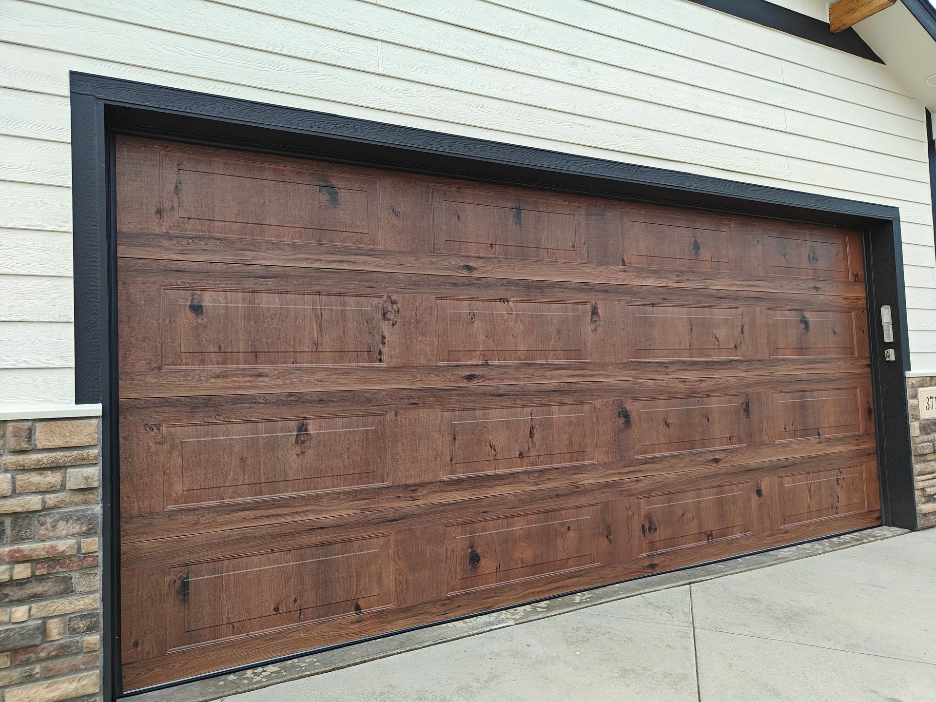 Brown wooden garage door on a light-sided house with stone trim, viewed at an angle