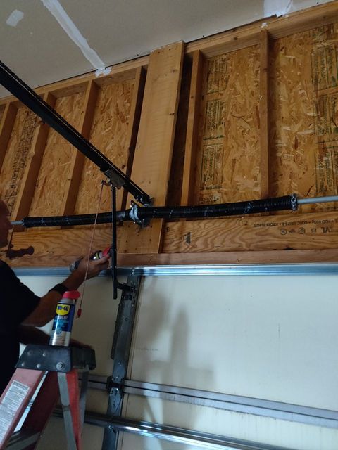 Person adjusting a garage door opener rail inside an unfinished garage with exposed wall studs