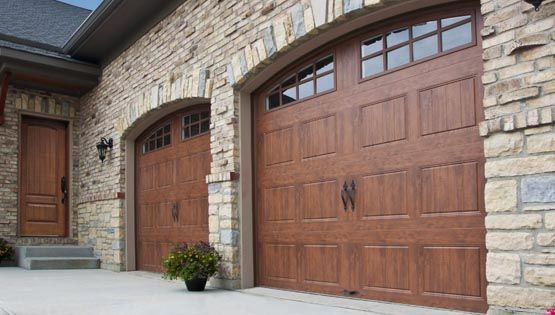 Stone house entrance with three wooden garage doors and a front door under an arched entryway