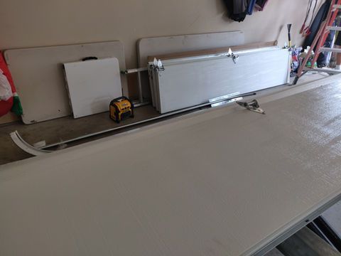 Garage with a large white panel or door section laid flat on the floor beside tools and materials.