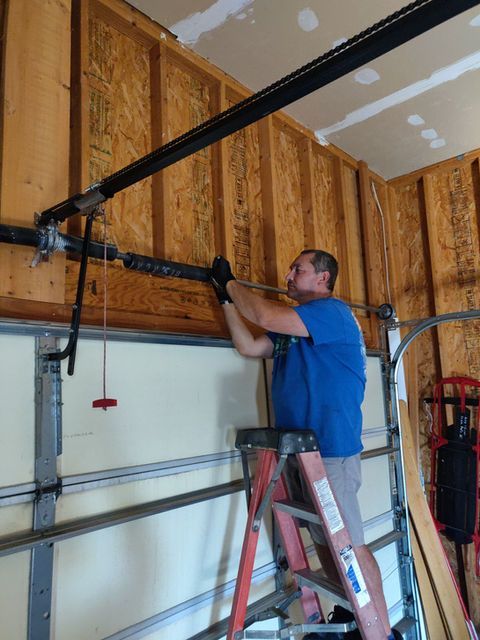 Man on ladder installing a garage door opener track inside an unfinished garage