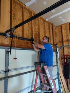Man in blue shirt installing a garage door opener with a ladder in a garage
