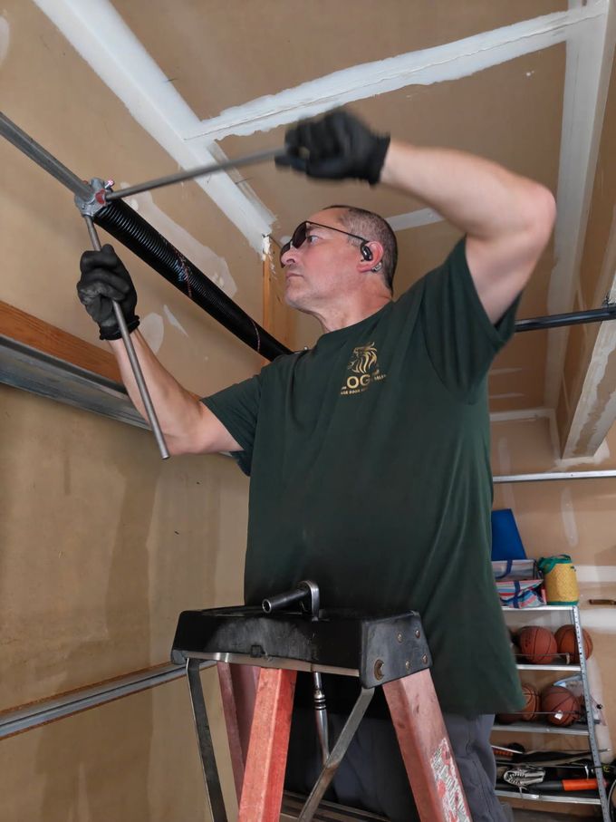 Man on a ladder installing a garage door opener on a wall-mounted track.