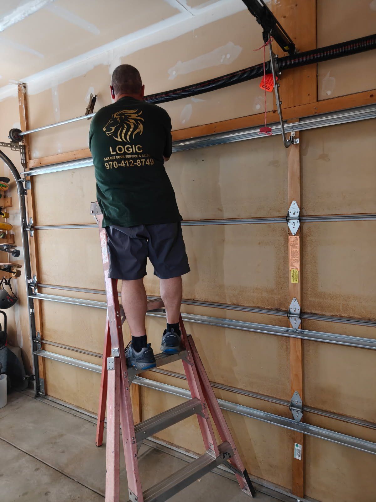 Person on a ladder adjusting wall framing in a garage with drywall seams visible