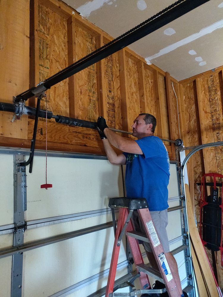Man adjusting a garage door opener track with a ladder in a garage interior