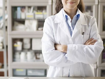 Una donna in camice è in piedi con le braccia incrociate in una farmacia.