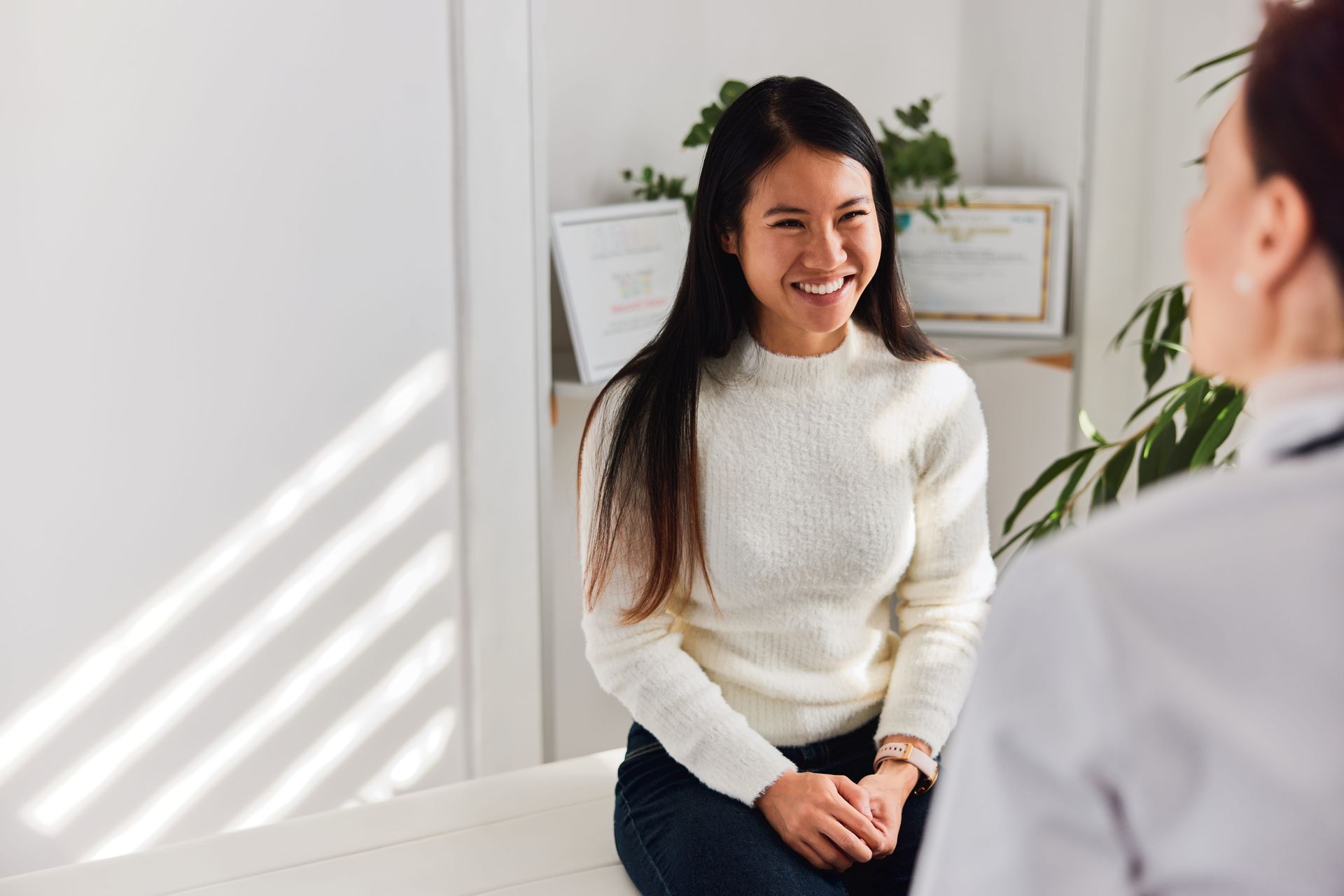 Woman smiling in a bright room, seated across from another person during a conversation