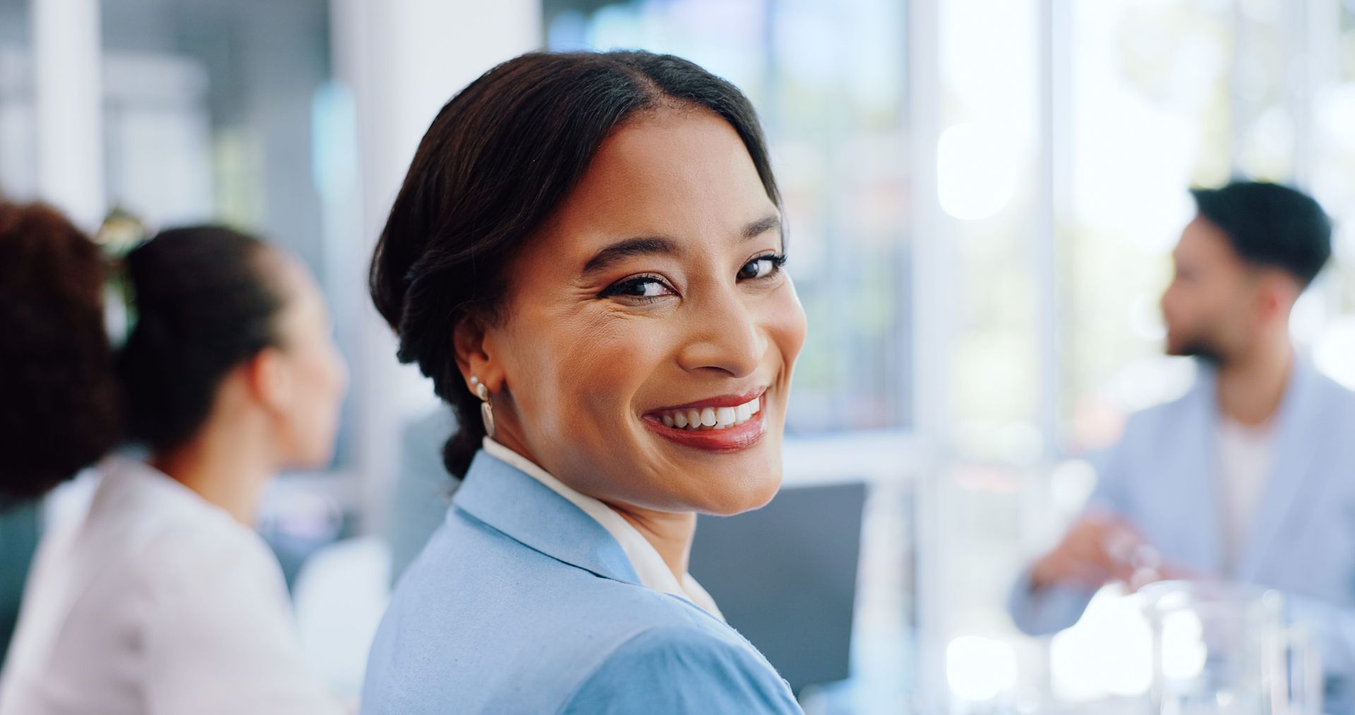 Woman smiling at a laptop on a wooden table in a bright room