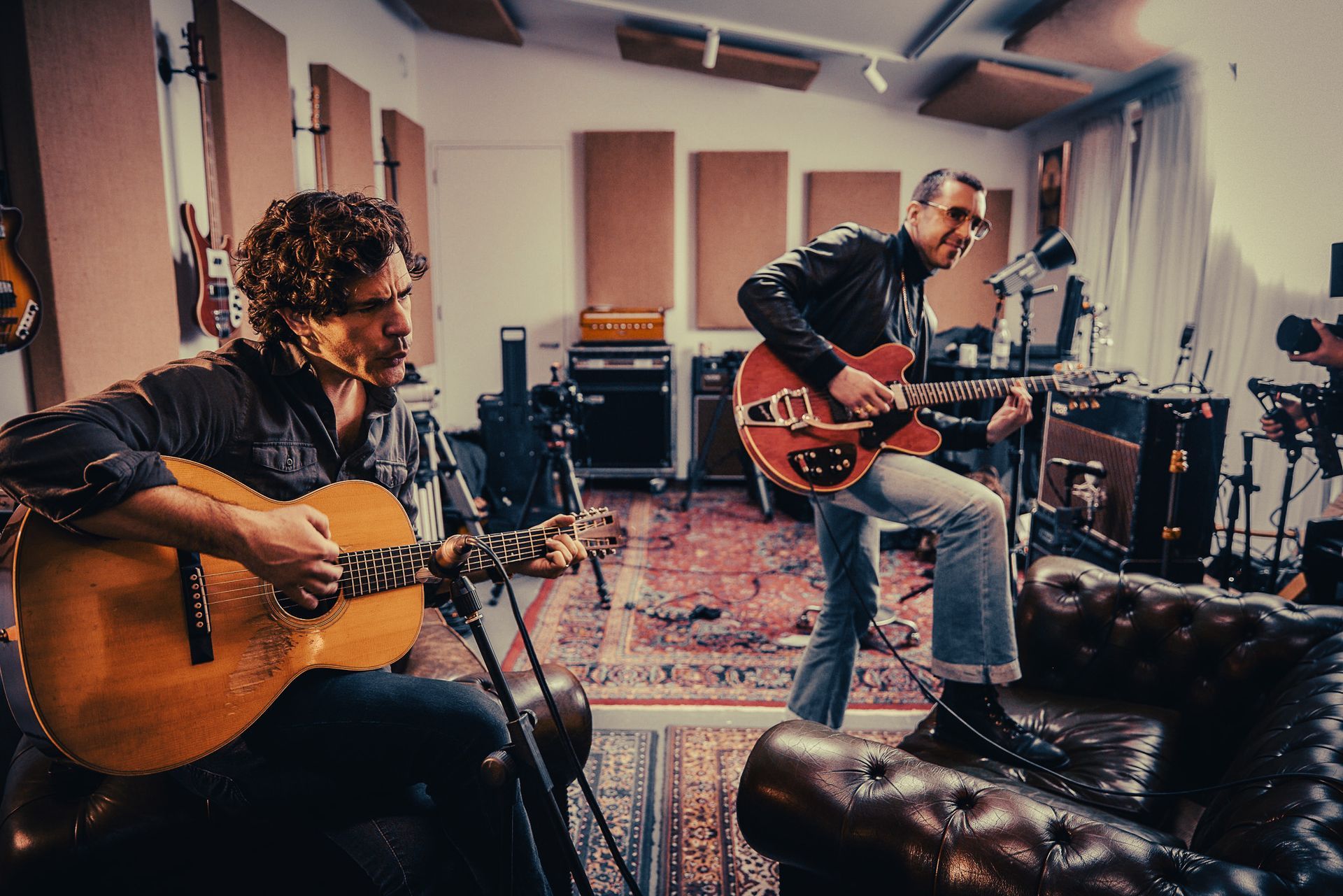 two men are playing guitars in a room .