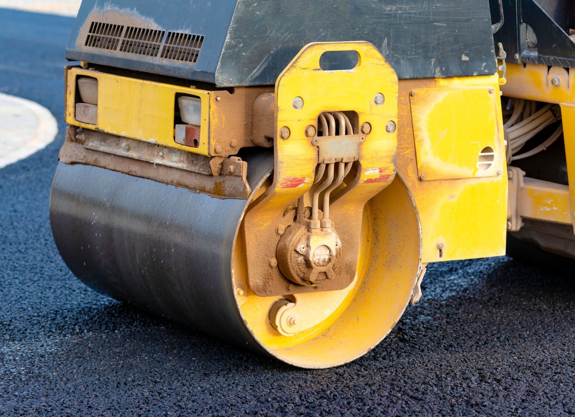 Yellow road roller compacting fresh asphalt pavement during construction, close-up of steel drum.