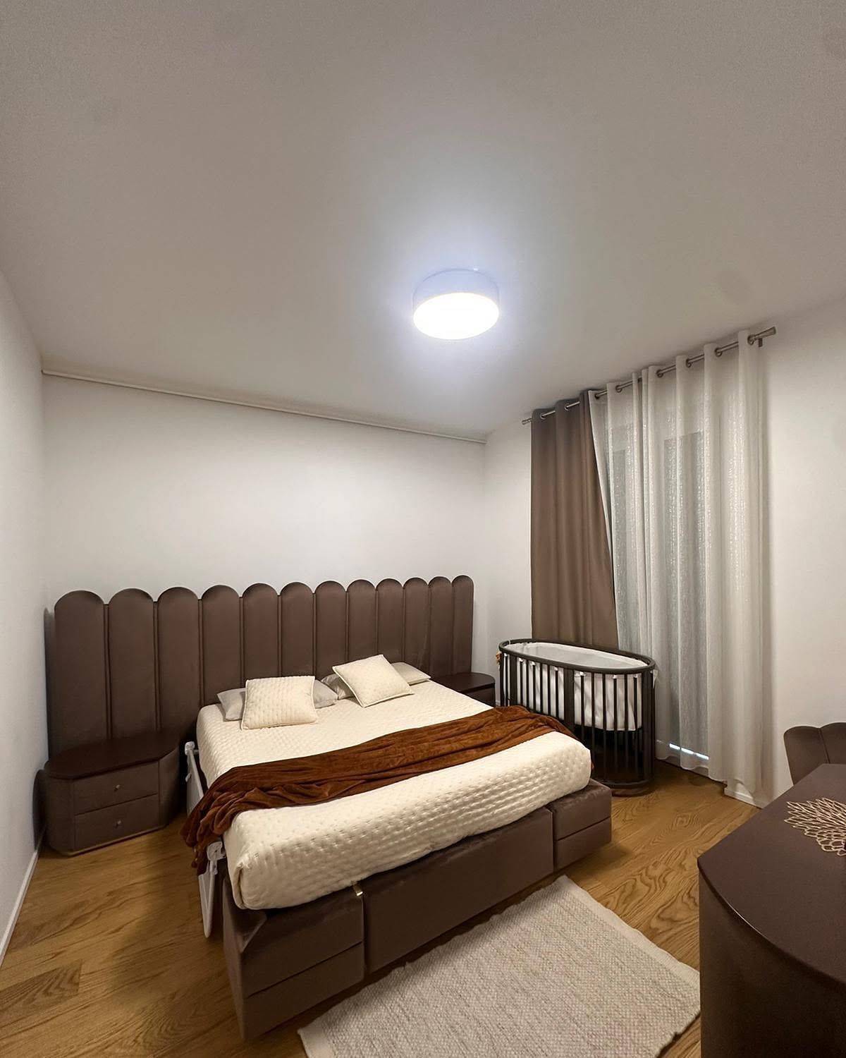 Accogliente camera da letto con un letto, tende, comodino e un caldo pavimento in legno sotto una plafoniera