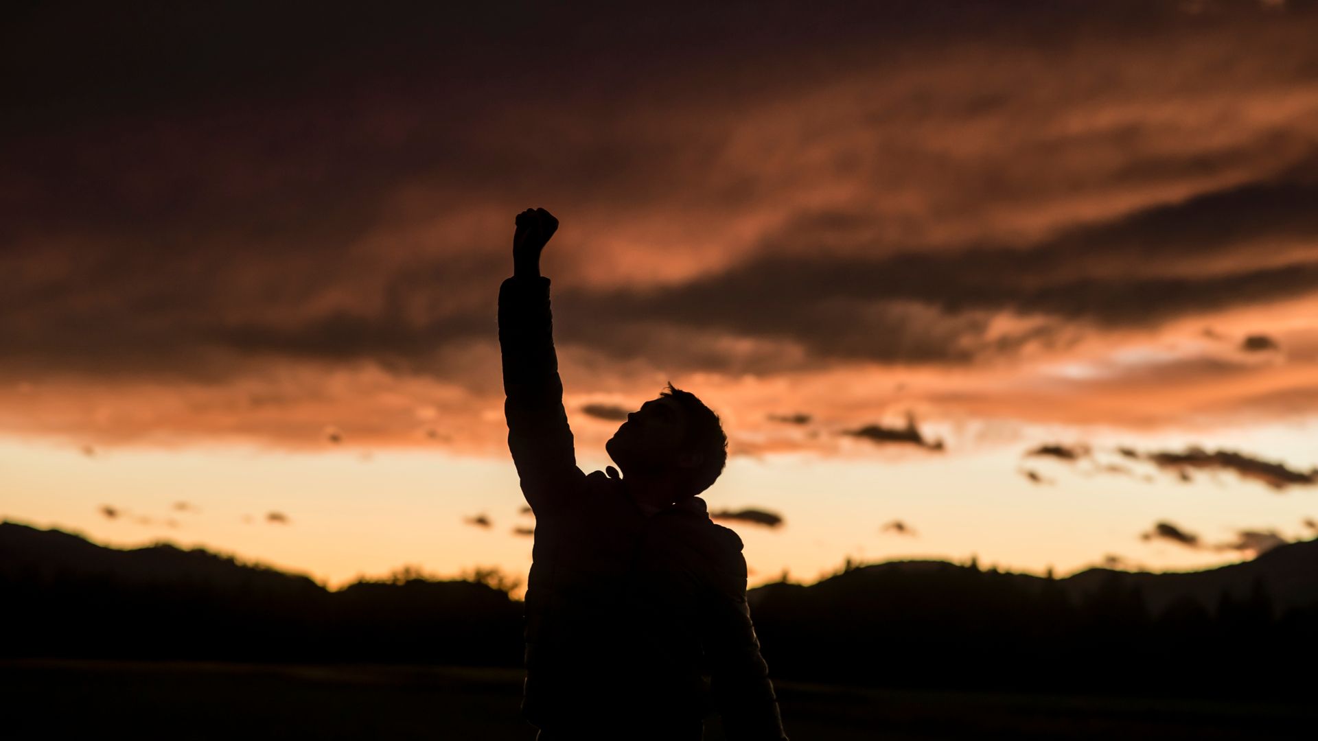 A person is raising their fist in the air at sunset.