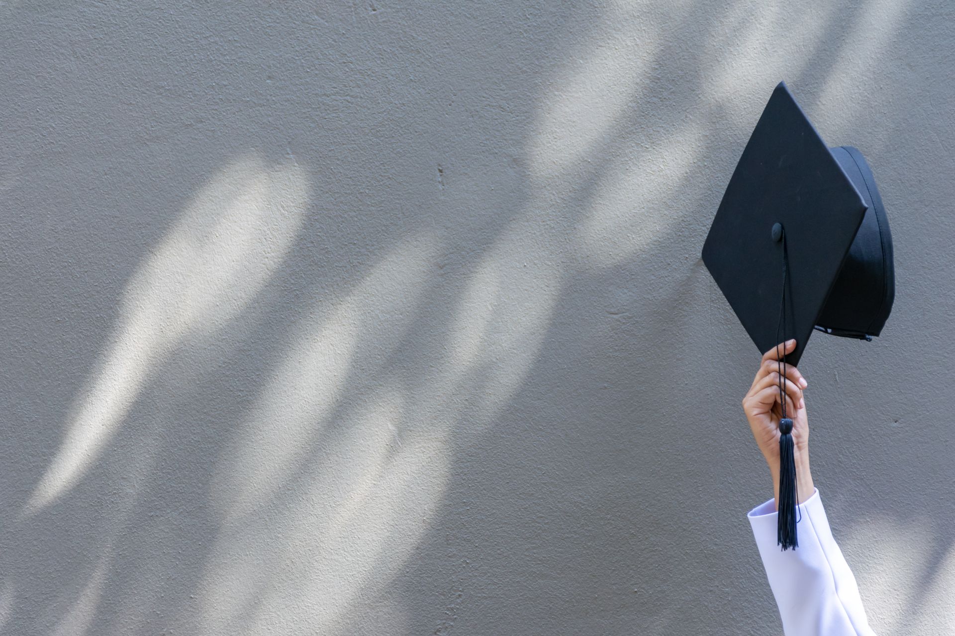 A person is holding a graduation cap in the air.