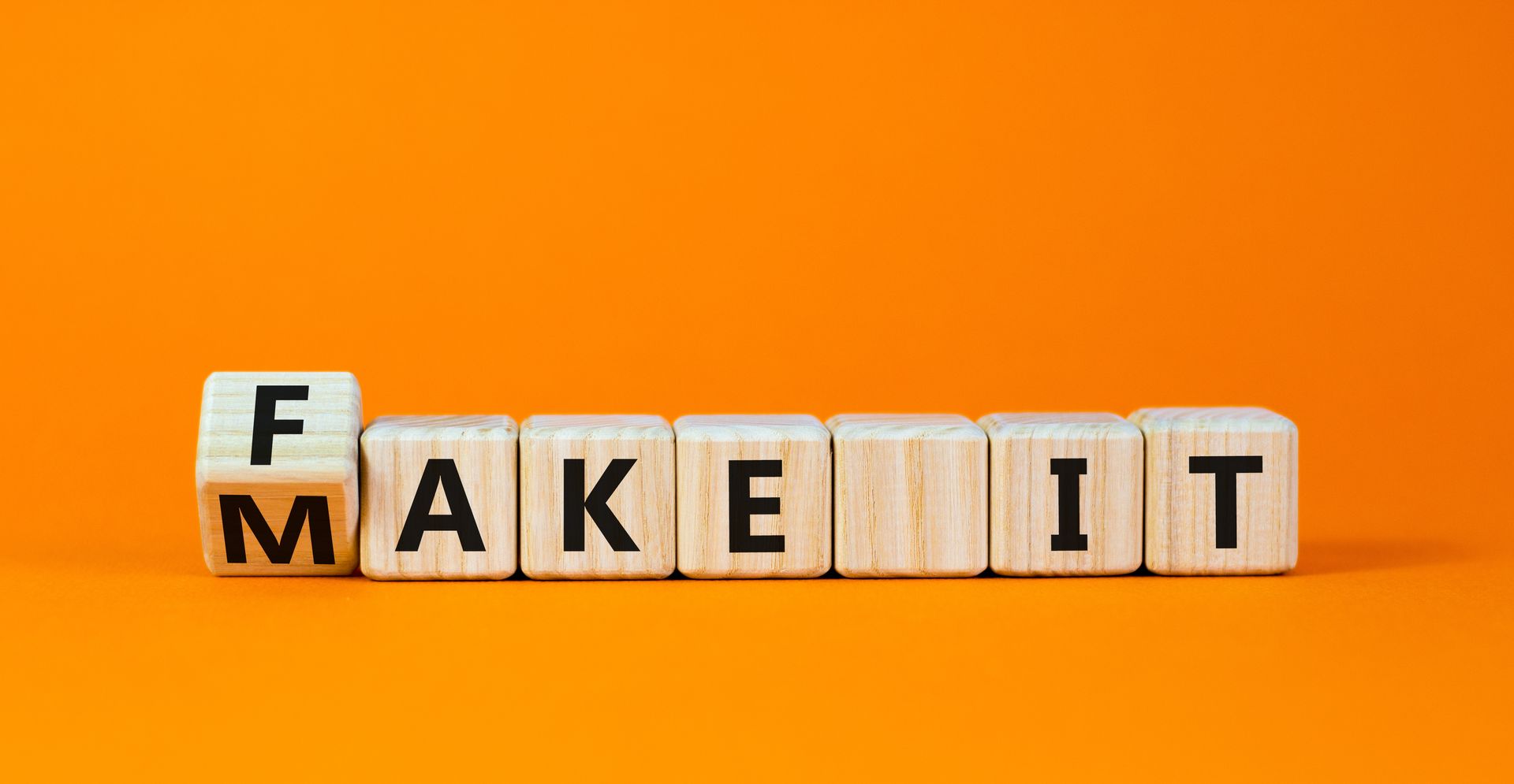The word fake it is written on wooden blocks on an orange background.