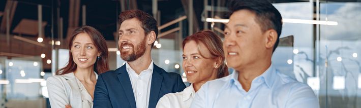 A group of business people are standing next to each other in an office and smiling.