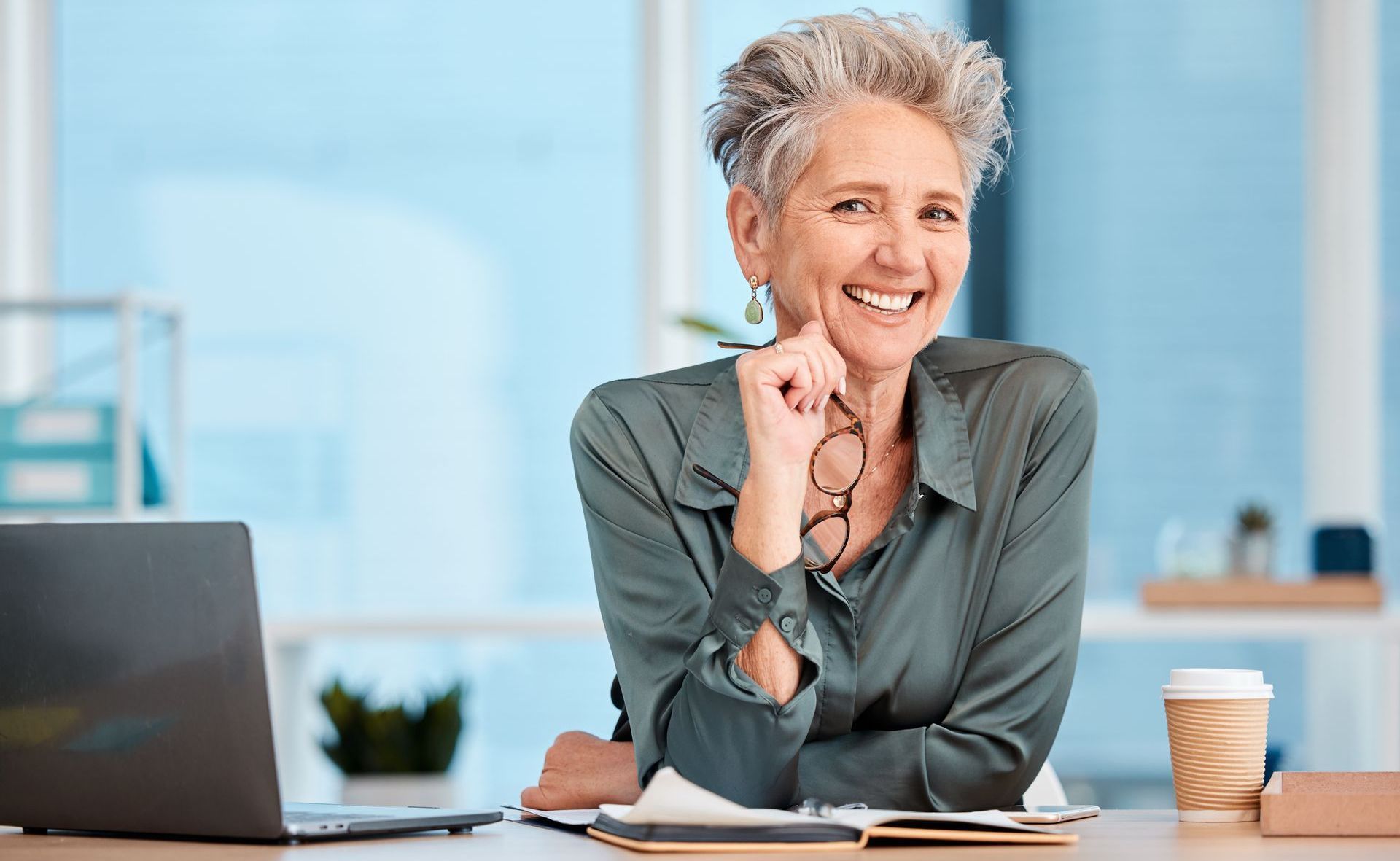 A woman is sitting at a desk with a laptop and a cup of coffee.