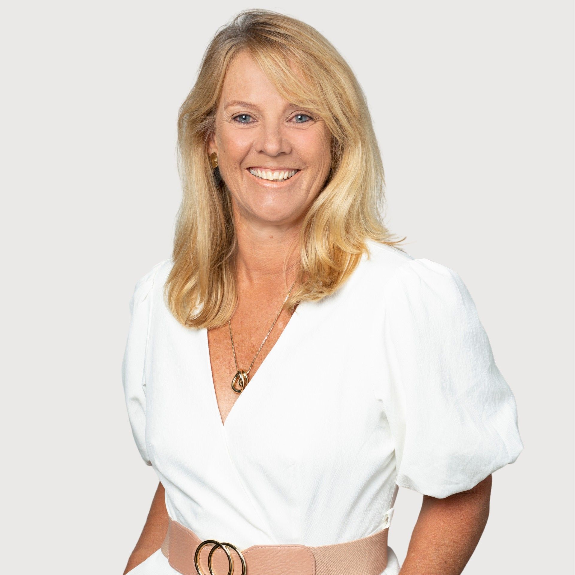 A woman wearing a white shirt and a pink belt is smiling for the camera.