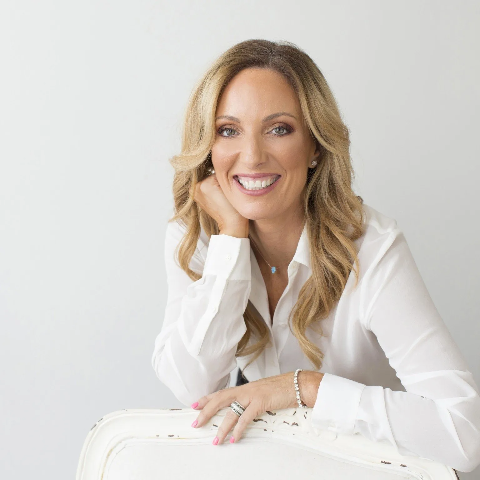 A woman in a white shirt is sitting in a white chair and smiling.