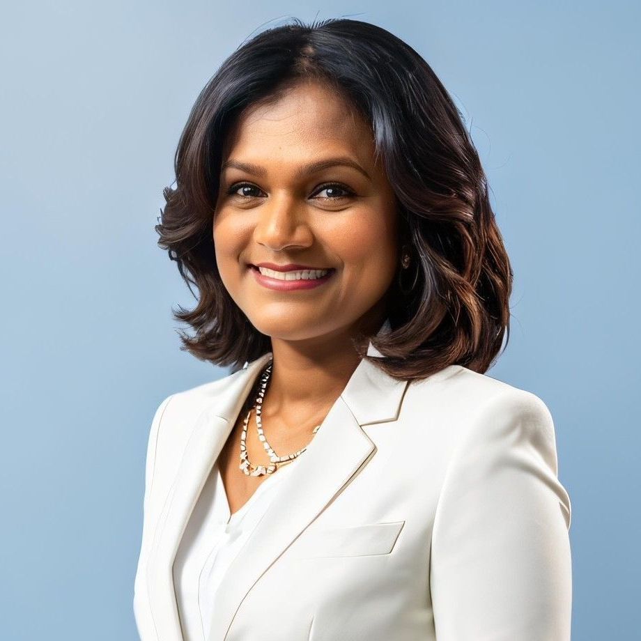 A woman wearing a white jacket and a pearl necklace is smiling for the camera.