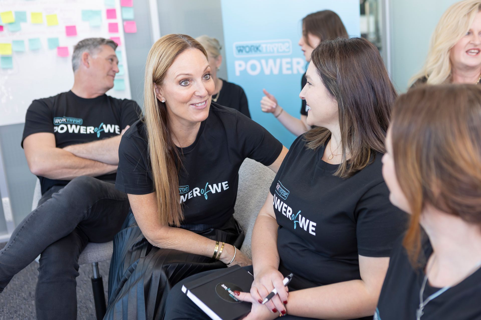 Group of people in black shirts, talking and gesturing in an office setting.