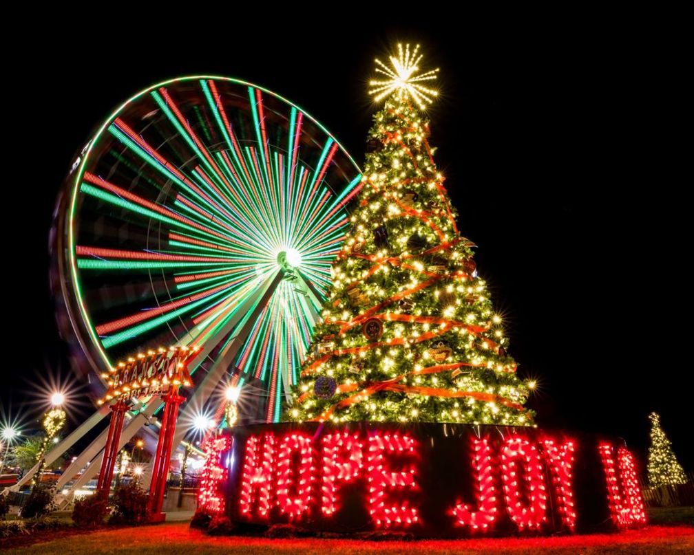 Ferris wheel and lit Christmas tree with glowing red “HOPE JOY” sign at night
